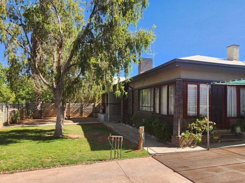 Rear view of the property featuring a brick facade, established lawn, concrete driveway, and chimney, showcasing the outdoor space and building exterior.