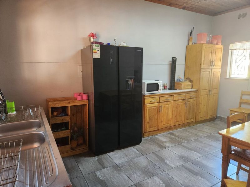 A functional kitchen featuring wooden cabinetry, tiled flooring, a double stainless steel sink, and a timber ceiling.
