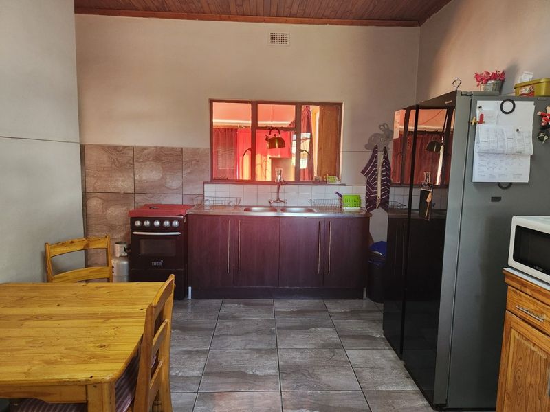 A functional kitchen featuring dark wood cabinetry, a double sink, tiled backsplash, and tiled flooring, complemented by a timber-paneled ceiling.