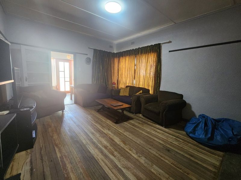 A living room featuring original hardwood flooring, a ceiling light fixture, and access to an adjacent room through a sliding door.