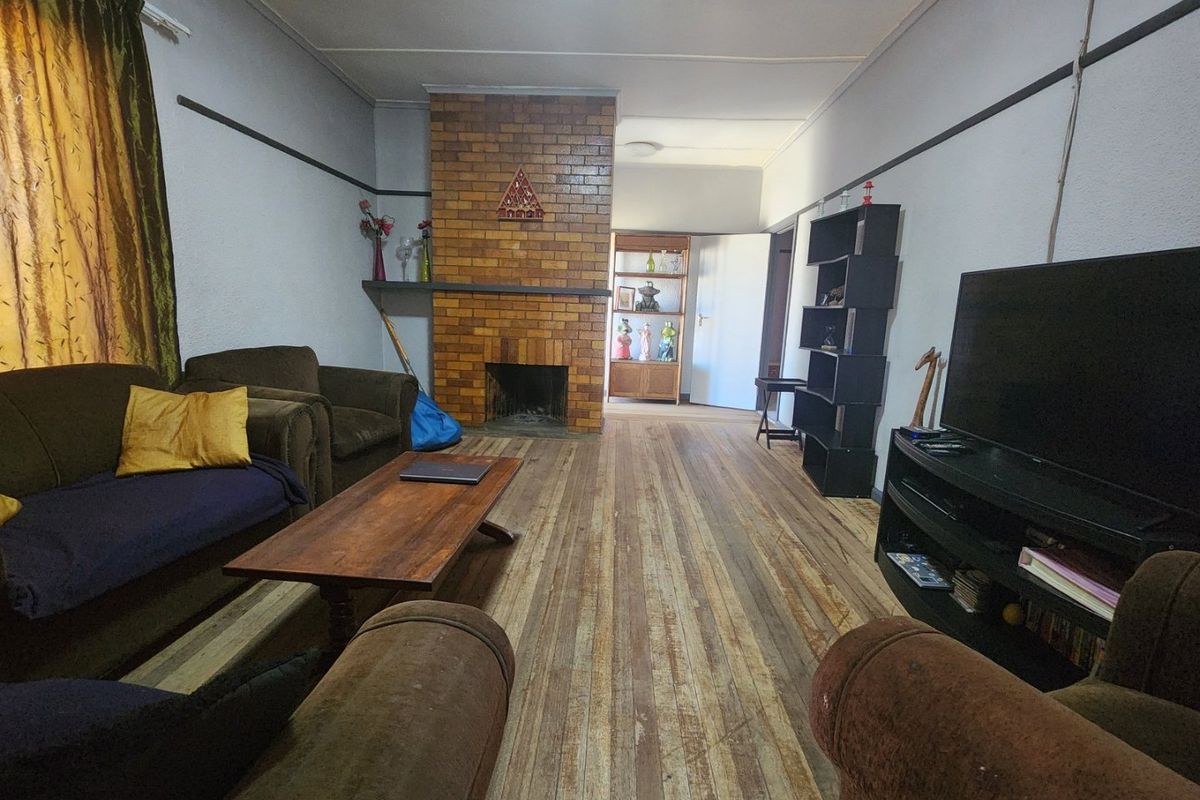 A living room featuring a central brick fireplace and original timber flooring, offering a classic layout with potential for cosmetic updates.