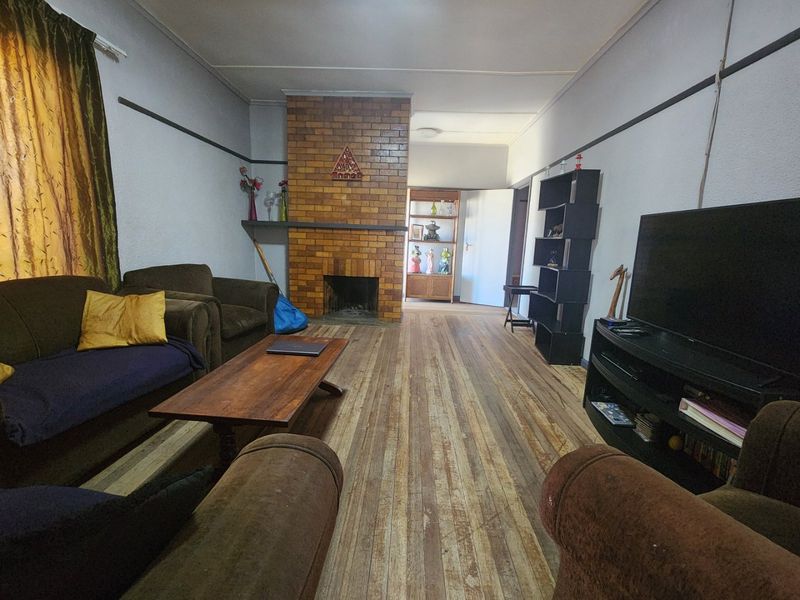 A living room featuring a central brick fireplace and original timber flooring, offering a classic layout with potential for cosmetic updates.