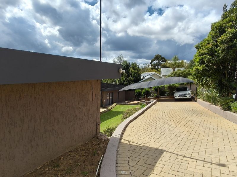A paved driveway leading to a carport, featuring a retaining wall and established garden landscaping.