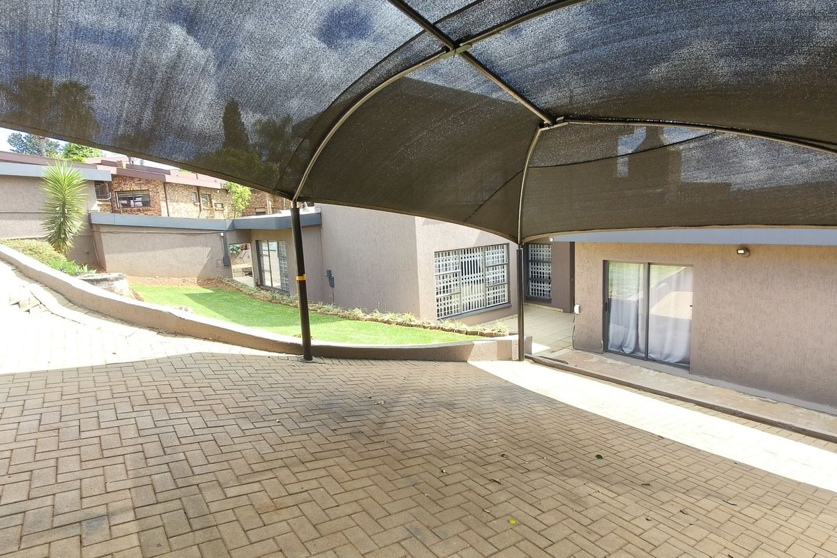 A paved rear courtyard area featuring a shade cloth carport, retaining wall, and access to the home via sliding glass doors.