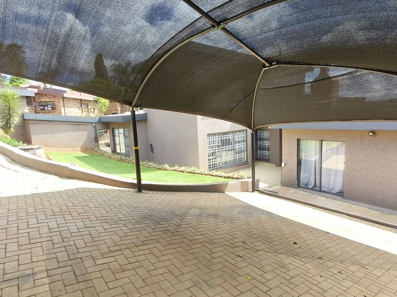 A paved rear courtyard area featuring a shade cloth carport, retaining wall, and access to the home via sliding glass doors.