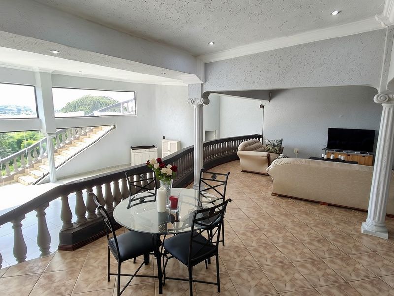 Spacious open-plan living and dining area featuring decorative columns, a classic balustrade, tiled flooring, and an integrated staircase overlooking the lower level.