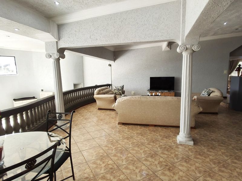 Spacious open-plan living area featuring decorative columns, a classic balustrade, and tiled flooring, offering a unique architectural layout.