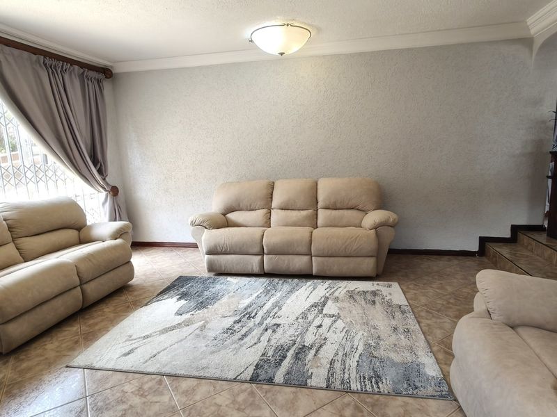 A spacious living room featuring tiled flooring, textured walls, and security bars on the windows, providing a functional and well-lit living area.