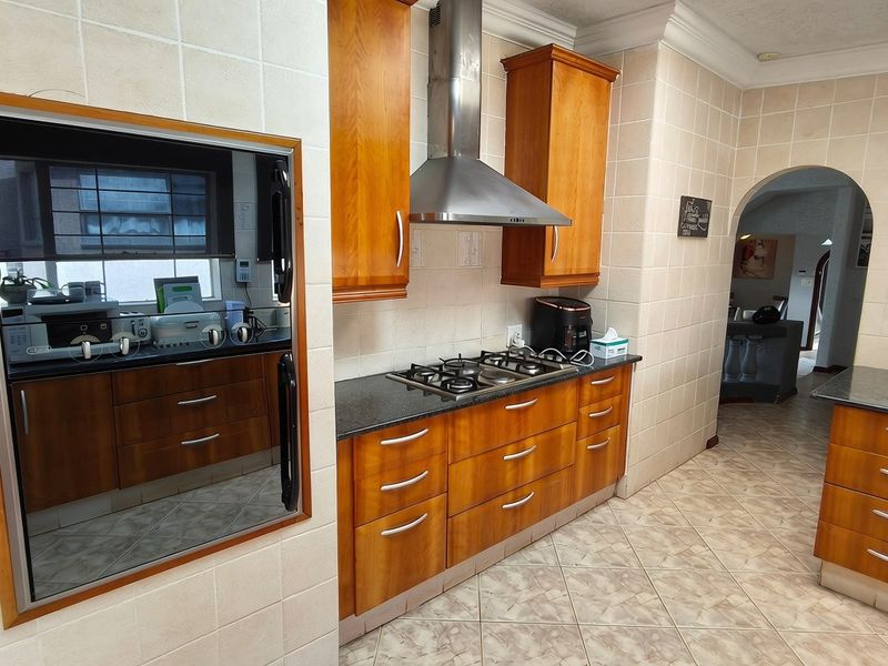 A functional kitchen featuring warm-toned wooden cabinetry, granite countertops, a gas hob with a stainless steel extractor, and classic tiled finishes throughout.