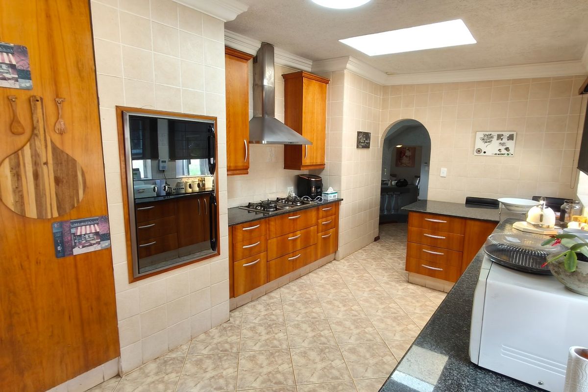 A functional kitchen featuring wooden cabinetry, granite countertops, a gas hob with extractor fan, built-in oven, and a skylight for natural lighting.