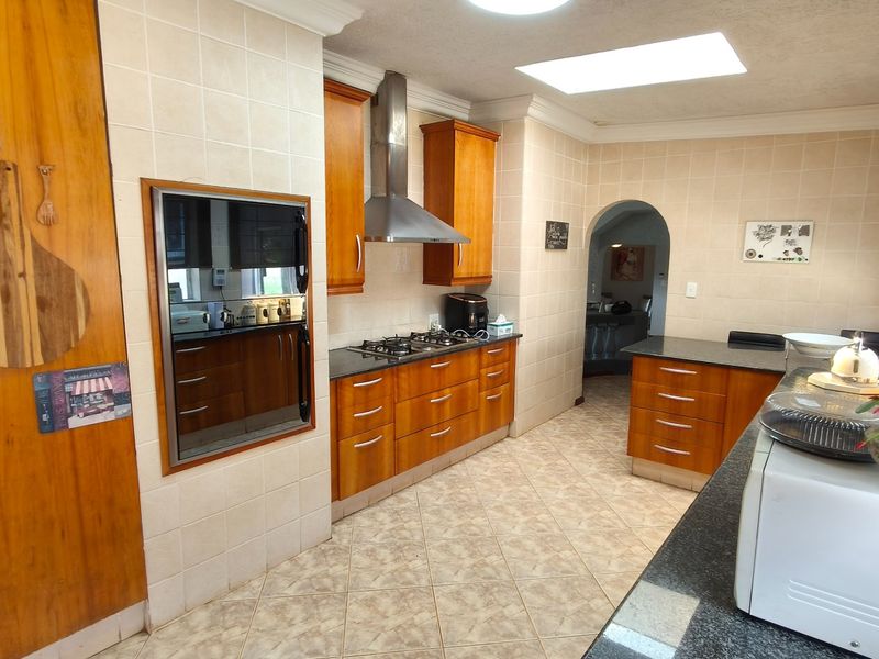 A functional kitchen featuring wooden cabinetry, granite countertops, a gas hob with extractor fan, built-in oven, and a skylight for natural lighting.