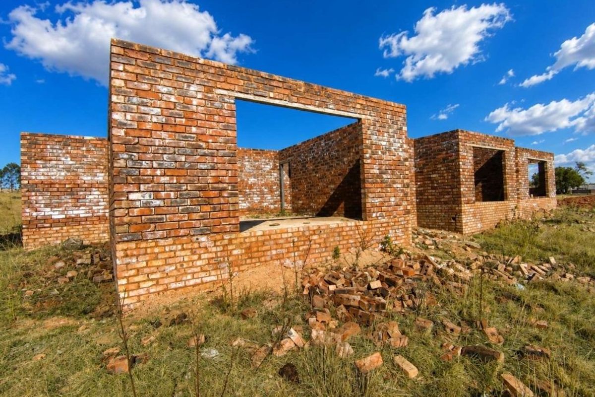 An unfinished brick structure showing the initial construction phase of a property on a rural farm plot.