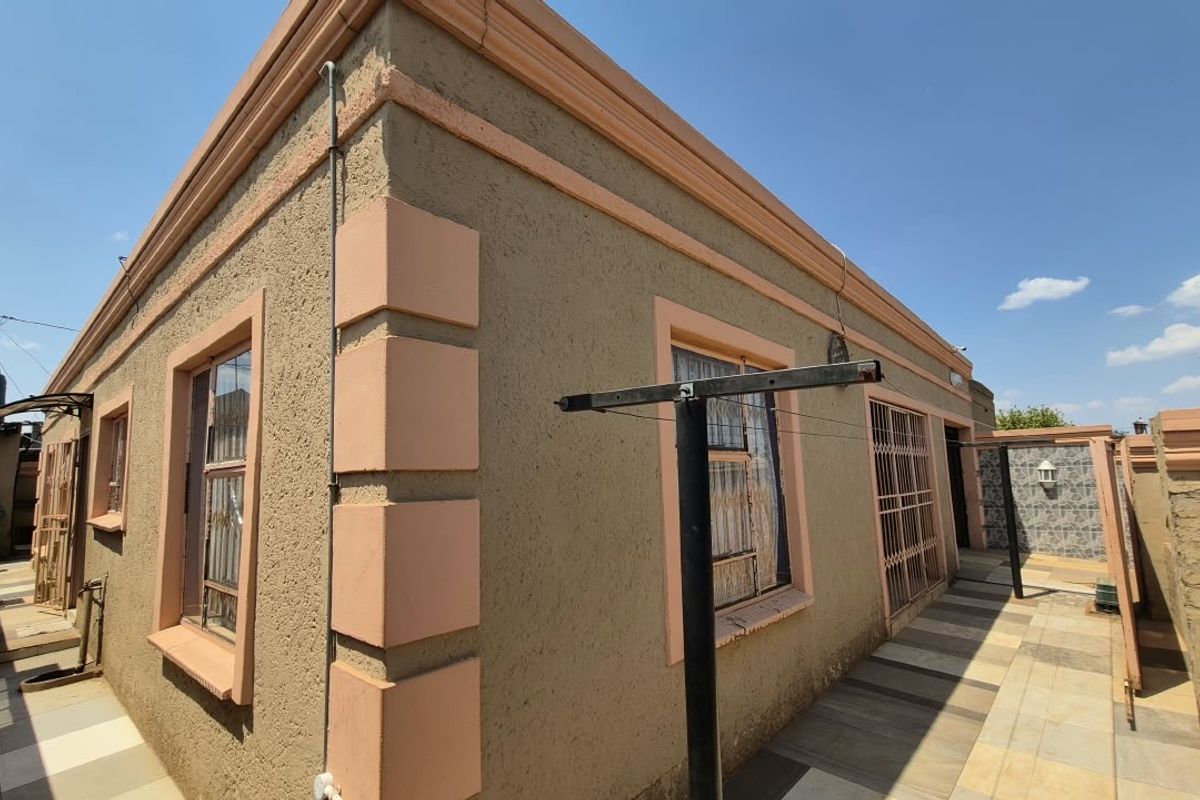 Rear exterior view of the house featuring a tiled patio area, security gates, and perimeter wall finishes.