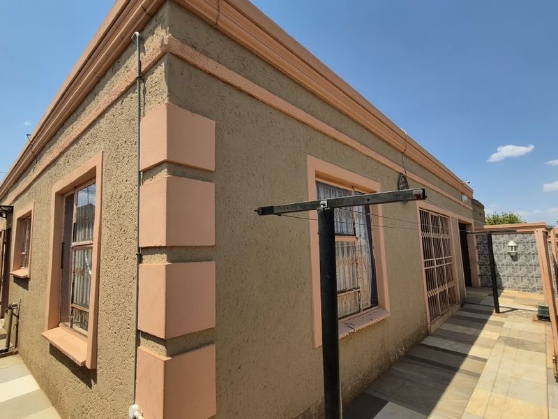Rear exterior view of the house featuring a tiled patio area, security gates, and perimeter wall finishes.