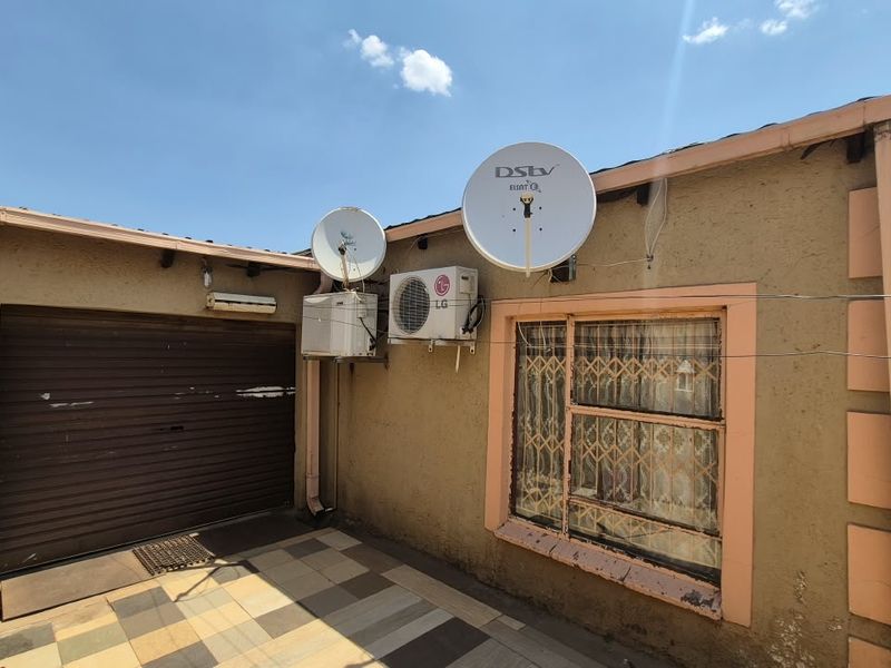 Rear exterior view featuring a tiled patio, roller garage door, and wall-mounted air conditioning units with satellite dishes.