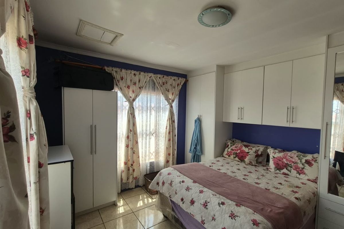 A bedroom featuring built-in cupboards, tiled flooring, and a mirrored wardrobe door, providing functional storage and a neutral base for updates.