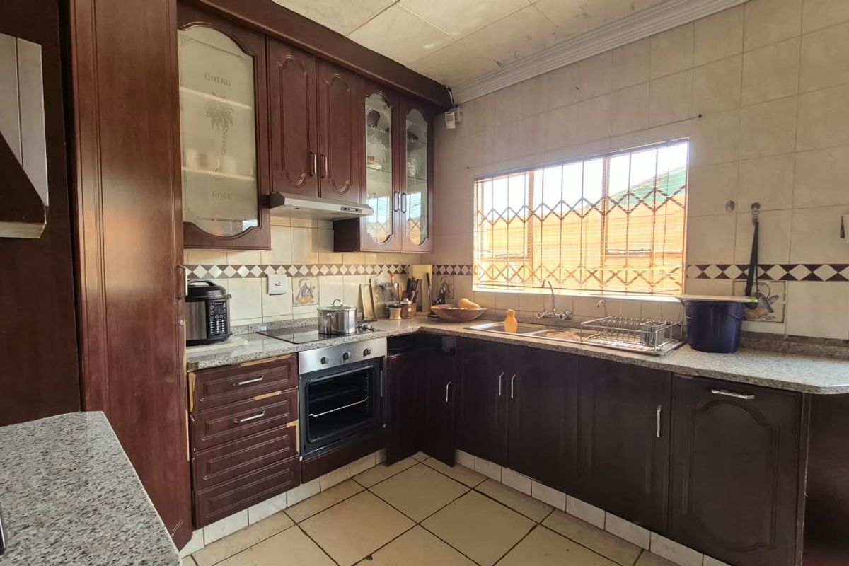 A functional kitchen featuring dark wood cabinetry, laminate countertops, built-in oven and hob, and tiled splashbacks, offering potential for a modern renovation.
