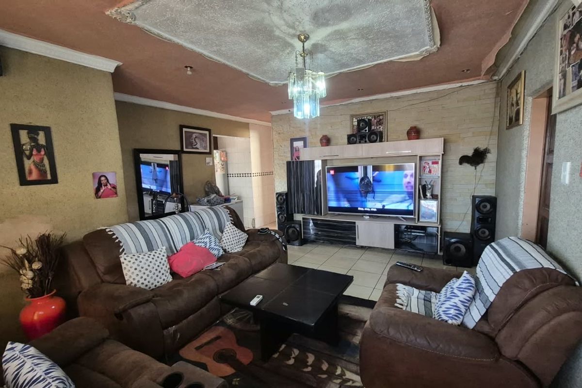 A living room featuring tiled flooring, a stone feature wall, and a built-in entertainment unit, with visible wear to the ceiling and wall finishes.