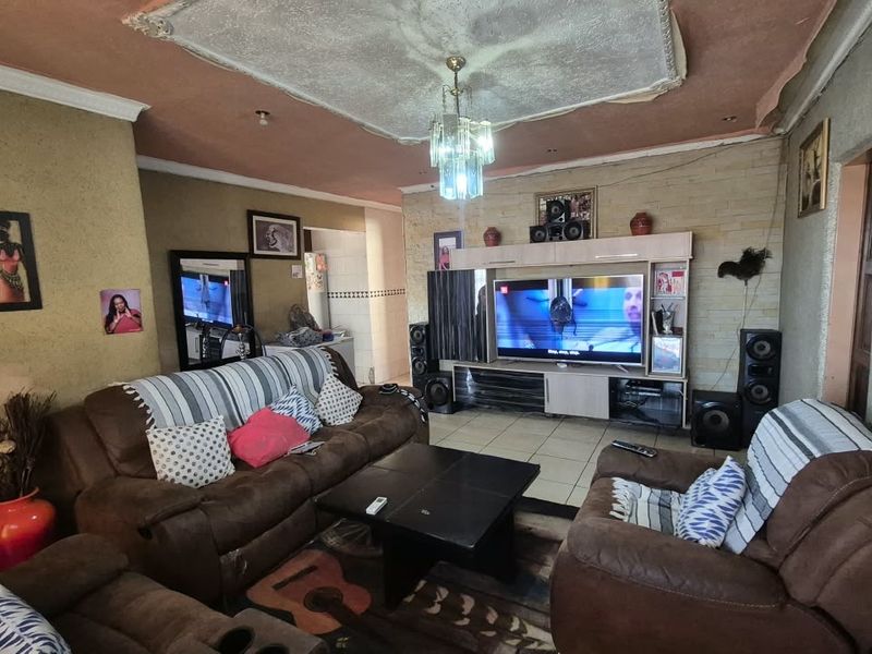 A living room featuring tiled flooring, a stone feature wall, and a built-in entertainment unit, with visible wear to the ceiling and wall finishes.