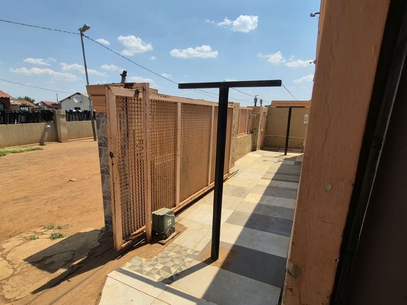 Front exterior area featuring a sliding gate with motor, tiled driveway section, and perimeter walling.