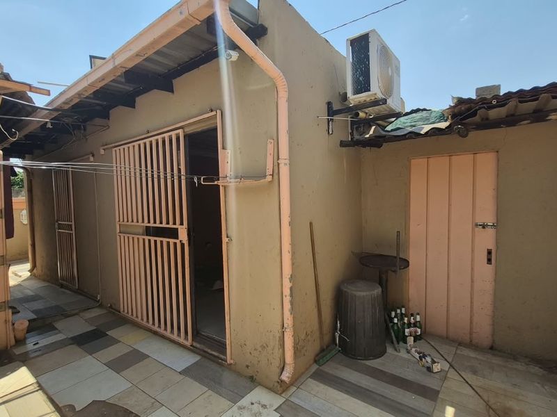 Rear exterior view of the property featuring a tiled patio area, security gates, and wall-mounted air conditioning unit with visible signs of weathering.