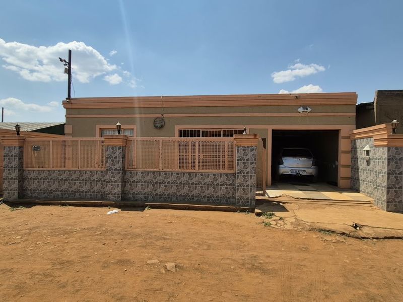 Front elevation of a single-story house featuring a perimeter wall with metal security gates, tiled accents, and an integrated garage.