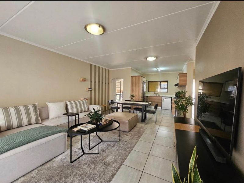 Spacious open-plan living and dining area featuring tiled flooring, neutral walls, and a functional kitchen with built-in cabinetry and integrated appliances.