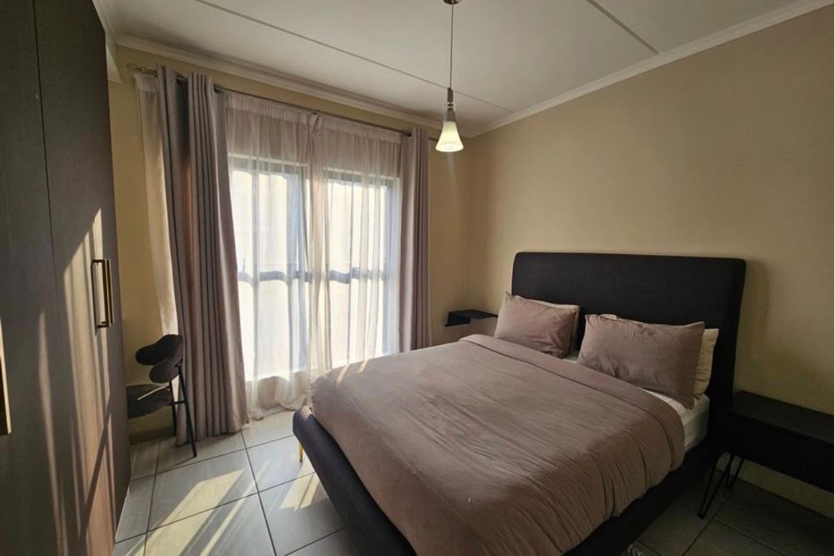 A well-lit bedroom featuring tiled flooring, a built-in wardrobe, and a large window with curtains, providing a comfortable and functional living space.