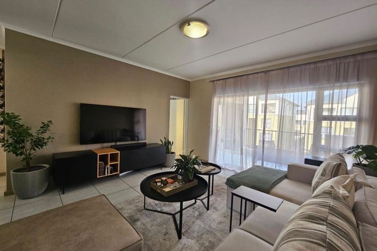 A well-maintained living room featuring tiled flooring, neutral wall tones, and a large sliding glass door providing access to the balcony.