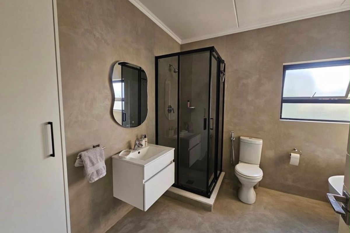 Modern bathroom featuring a sleek wall-mounted vanity, a contemporary shower enclosure with black framing, and a neutral cement-look wall finish.