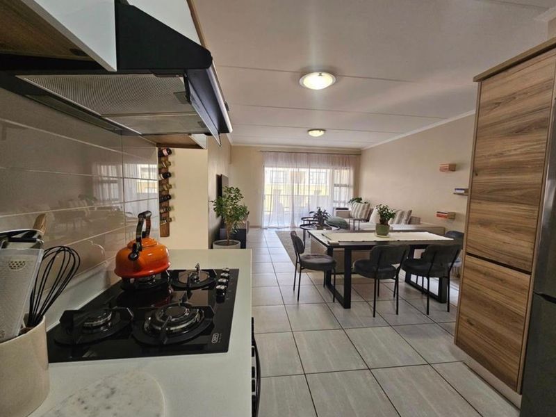Modern open-plan living area featuring a well-appointed kitchen with built-in cabinetry and gas hob, flowing seamlessly into a bright dining and lounge space.