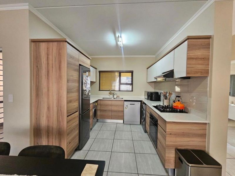 Modern galley-style kitchen featuring wood-grain cabinetry, light countertops, tiled flooring, and integrated appliances including a gas hob and oven.