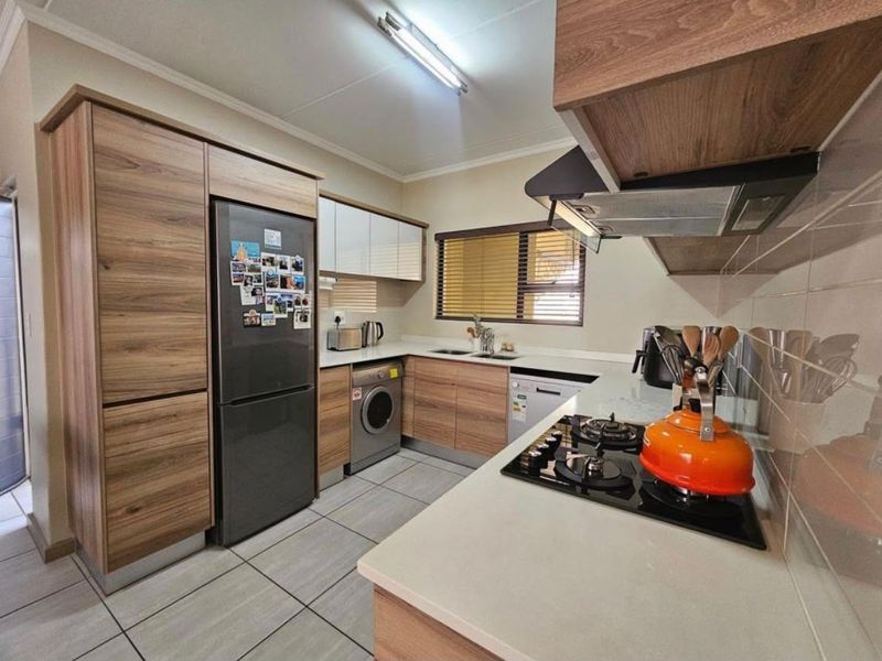 A modern, well-maintained kitchen featuring wood-finish cabinetry, a gas hob with extractor fan, tiled flooring, and a functional layout with integrated appliance spaces.