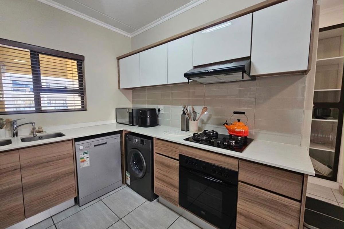 Modern kitchen featuring wood-grain cabinetry, stone countertops, integrated gas hob, oven, extractor fan, and tiled flooring with a neutral backsplash.