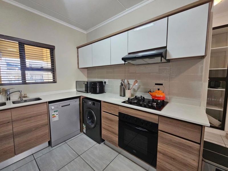 Modern kitchen featuring wood-grain cabinetry, stone countertops, integrated gas hob, oven, extractor fan, and tiled flooring with a neutral backsplash.