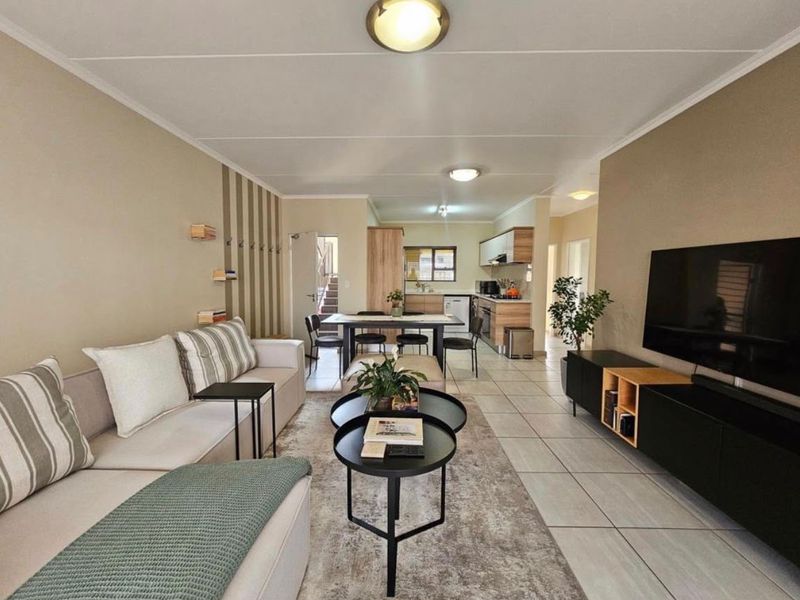 An open-plan living and dining area featuring tiled floors, neutral wall tones, and a functional kitchen space with built-in cabinetry.