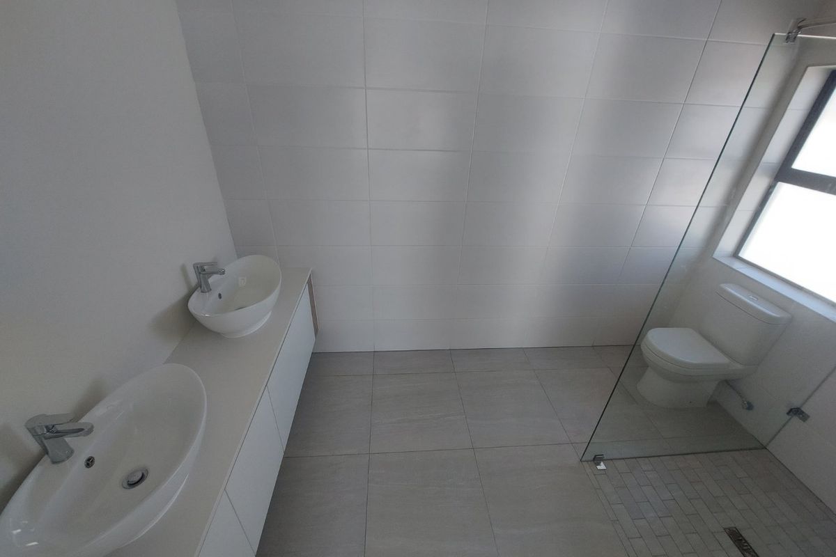 Modern bathroom featuring a double vanity with vessel sinks, a walk-in shower with a glass screen, and neutral floor-to-ceiling tiling.