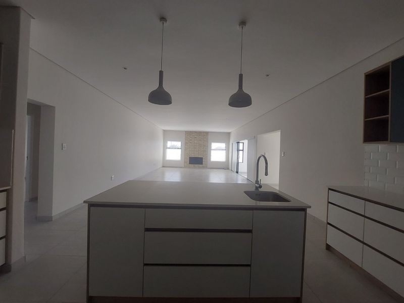 Spacious open-plan living area featuring a modern kitchen island with sink, tiled flooring, and a central fireplace with stone feature wall.