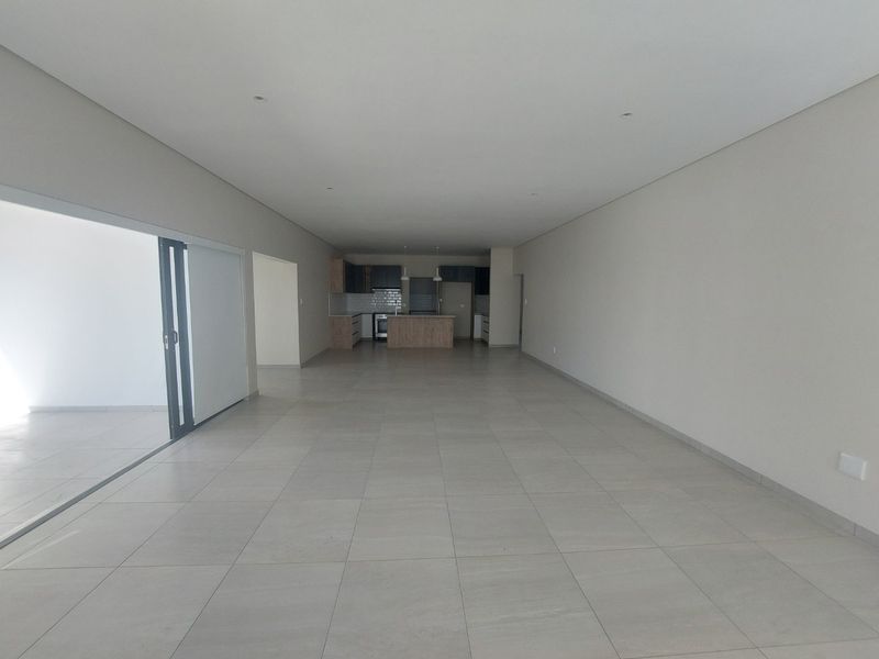 Spacious open-plan living and kitchen area featuring neutral tiled flooring, recessed lighting, and a modern kitchen with built-in cabinetry and island.