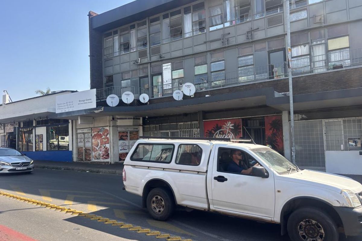 Street-level view of a multi-story commercial building featuring ground-floor retail shopfronts and upper-level office or residential windows with multiple satellite dishes.