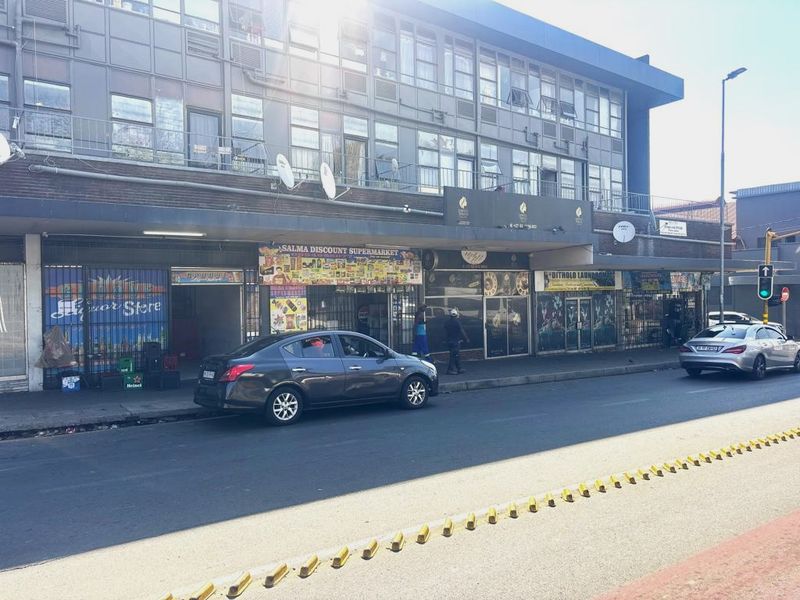 A multi-level commercial building featuring ground-floor retail storefronts with security gates and upper-level office or residential windows along a busy street.