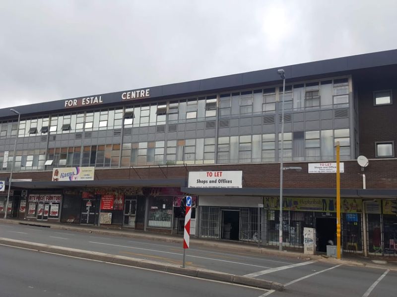 A multi-story commercial building featuring ground-level retail storefronts with a covered walkway and upper-level office windows, located along a busy street.
