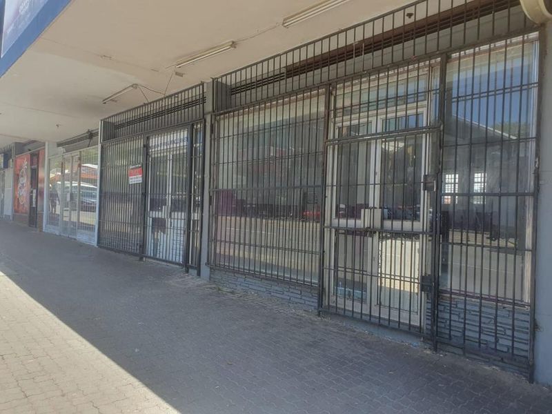Commercial storefront featuring large glass windows protected by security bars, situated along a paved sidewalk with overhead lighting.