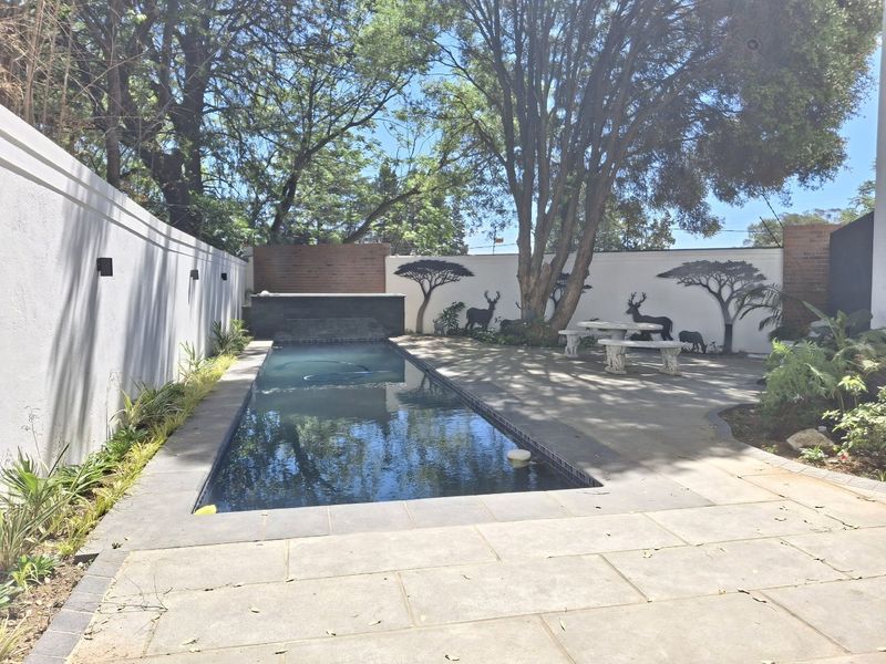 A well-maintained outdoor pool area featuring a rectangular swimming pool, paved patio space, and decorative boundary walls with integrated lighting.