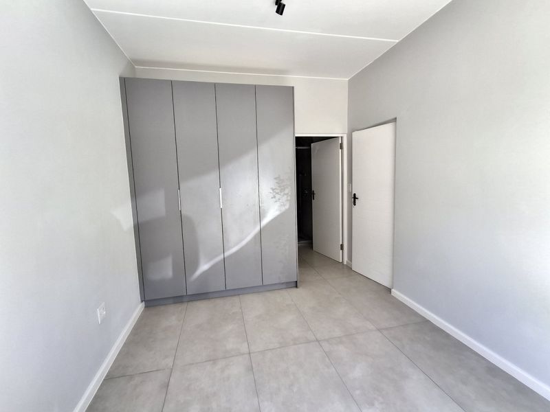 A clean, modern bedroom featuring neutral grey tiled flooring and sleek built-in cupboards, offering a bright and versatile space ready for personalization.