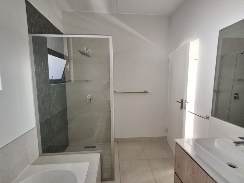 Modern bathroom featuring a glass-enclosed shower with dark accent tiling, a contemporary vessel sink vanity, and neutral floor tiles.