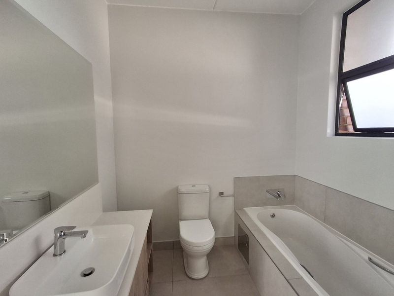 A clean, modern bathroom featuring a built-in vanity with a ceramic basin, a bathtub with chrome fixtures, and a large wall-mounted mirror.