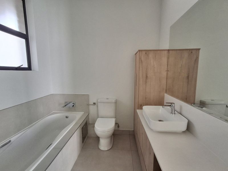 A clean, modern bathroom featuring a built-in bathtub, a contemporary vessel sink with vanity storage, and a large wall-mounted mirror.
