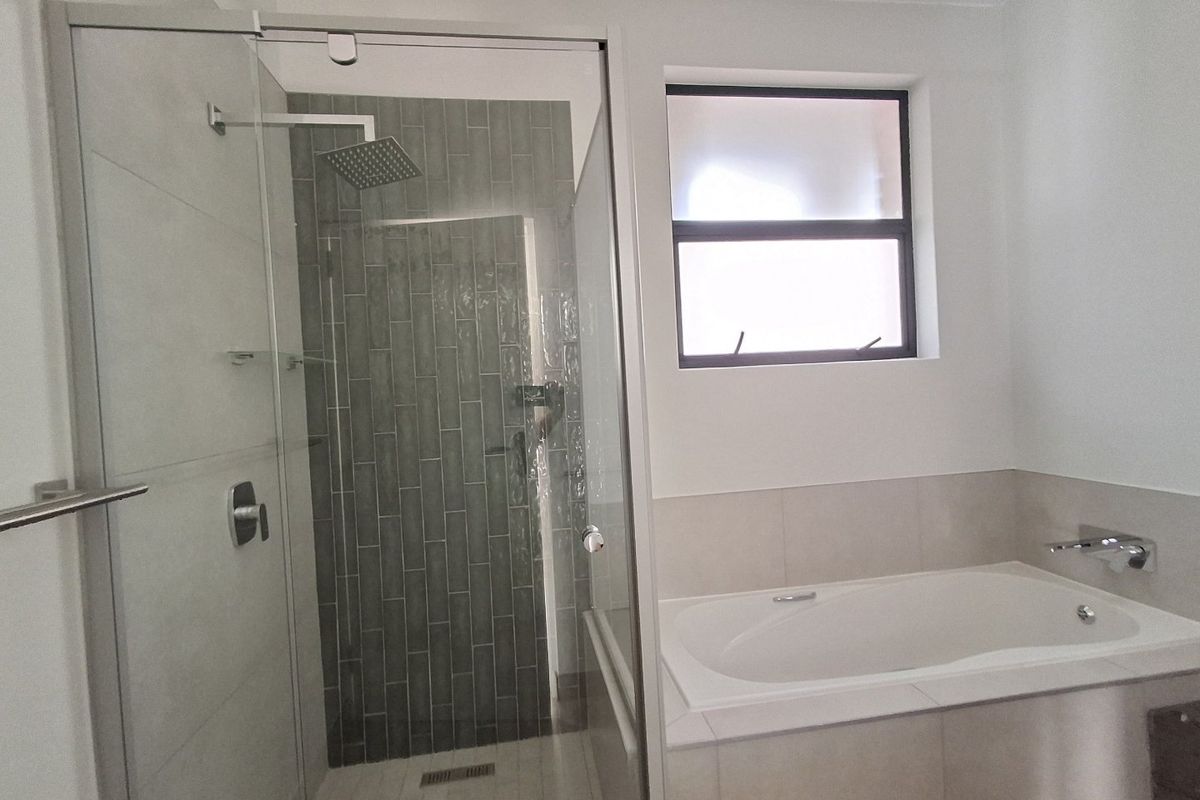 Modern bathroom featuring a glass-enclosed shower with a rain shower head and a built-in bathtub with neutral tiling.