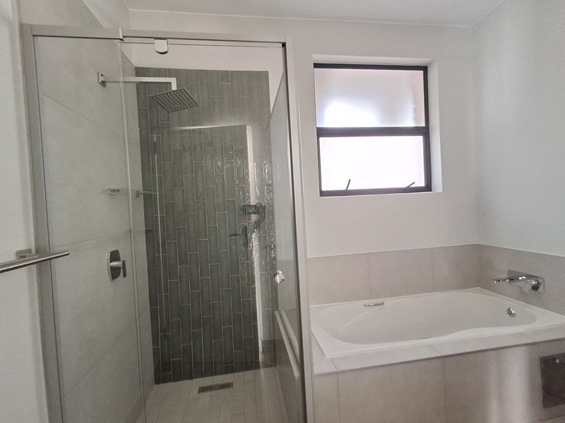 Modern bathroom featuring a glass-enclosed shower with a rain shower head and a built-in bathtub with neutral tiling.